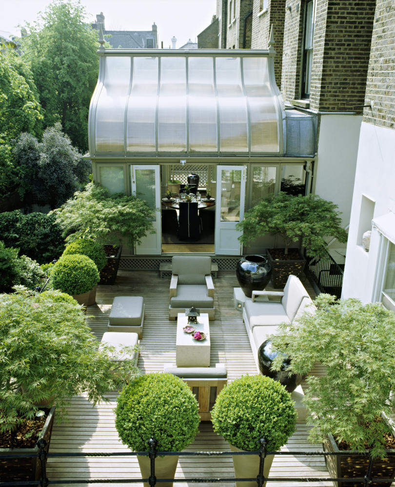 A modern town garden roof terrace with decked patio area table and chairs trees and shrubs in containers